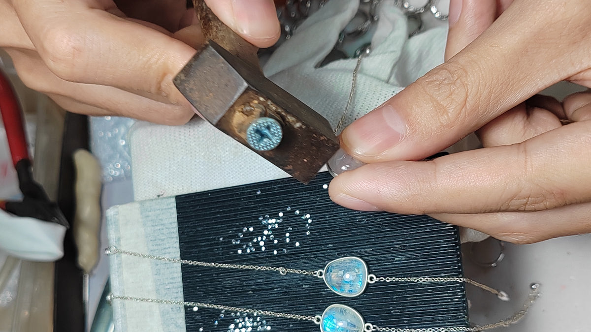 A wooden pusher pressing the silver bezel around a moonstone, with two finished bracelets on the tray below