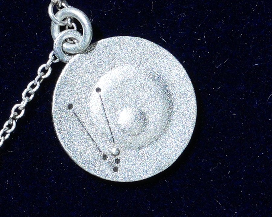 A silver coin close up, engraved with a constellation