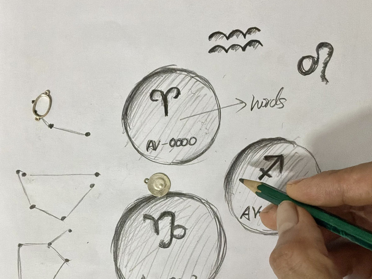 A hand sketching constellation designs beside a blank coin