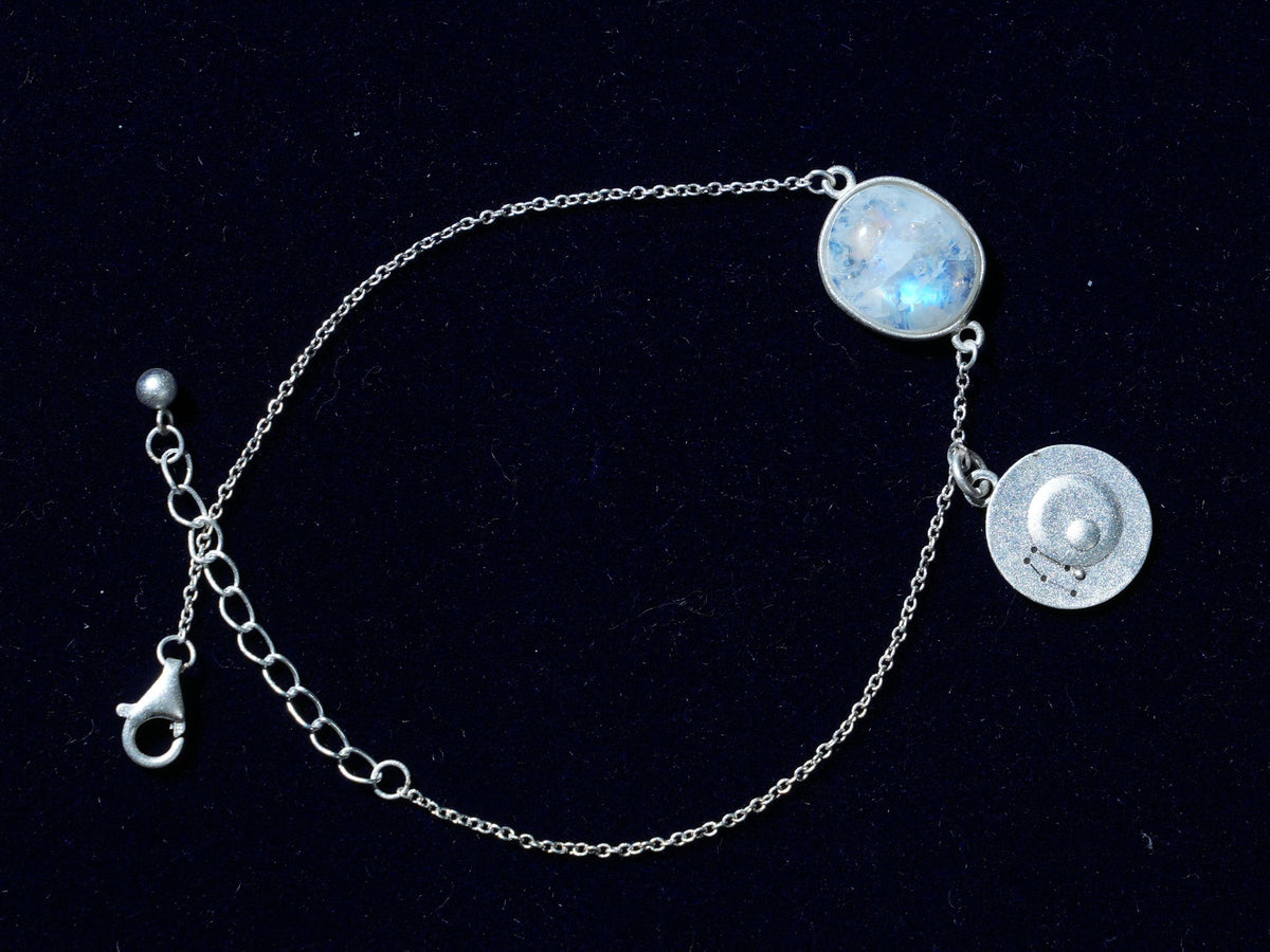 A rainbow moonstone bracelet with its coin, laid flat on navy velvet