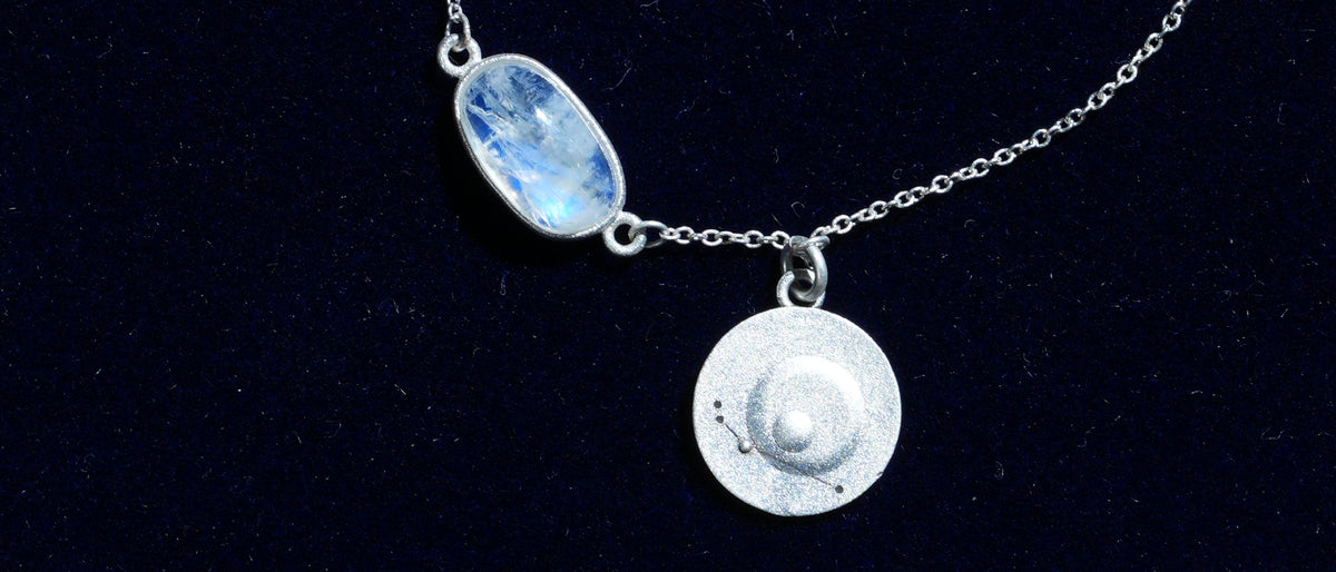 Close-up of a rainbow moonstone bracelet: the stone and its engraved coin on navy velvet