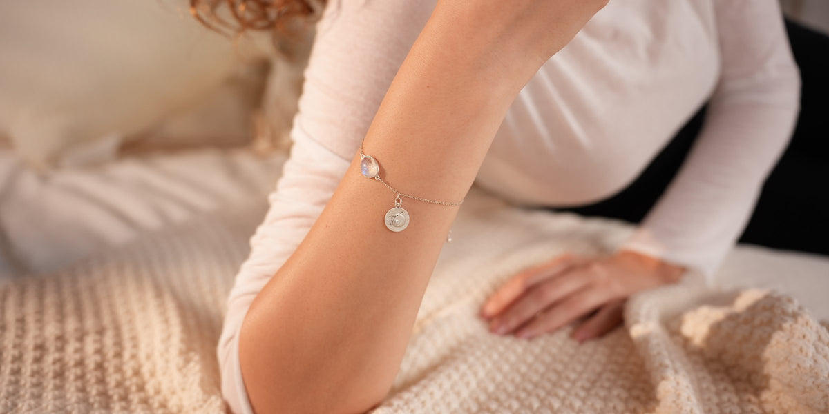 Rainbow moonstone and engraved coin bracelet on a wrist, resting on a cream knitted blanket