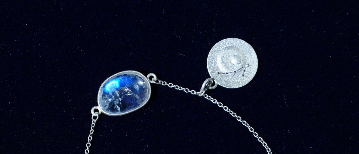 Close-up of the Pisces piece: a natural rainbow moonstone and its constellation coin on navy velvet