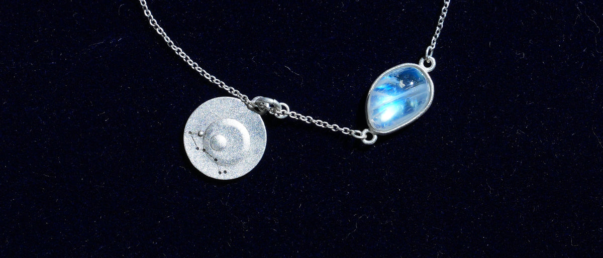 Close-up of the Scorpio piece: a natural rainbow moonstone and its constellation coin on navy velvet
