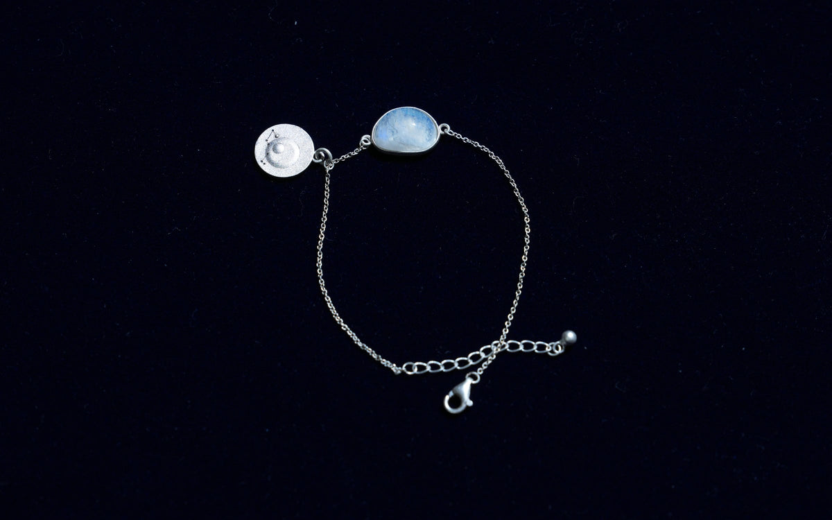 A rainbow moonstone bracelet with an engraved silver coin, laid flat on dark velvet