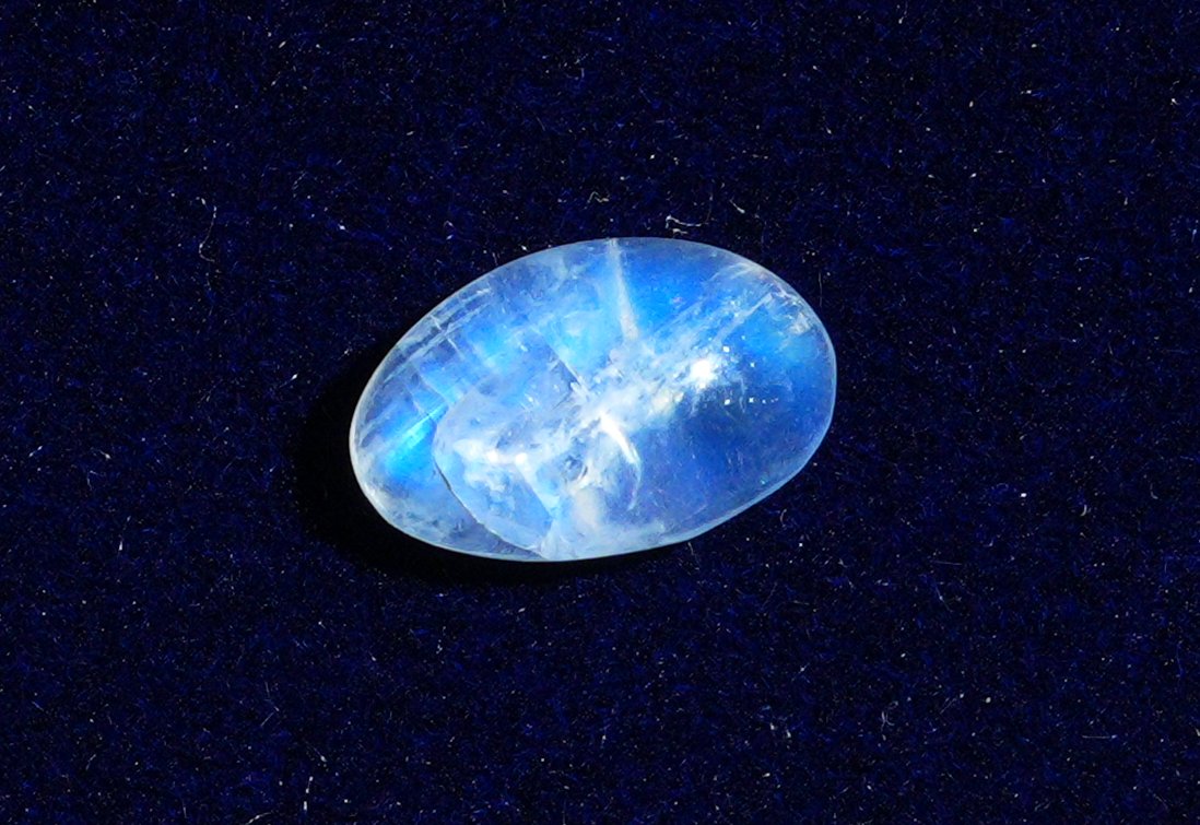 A single natural moonstone on navy velvet